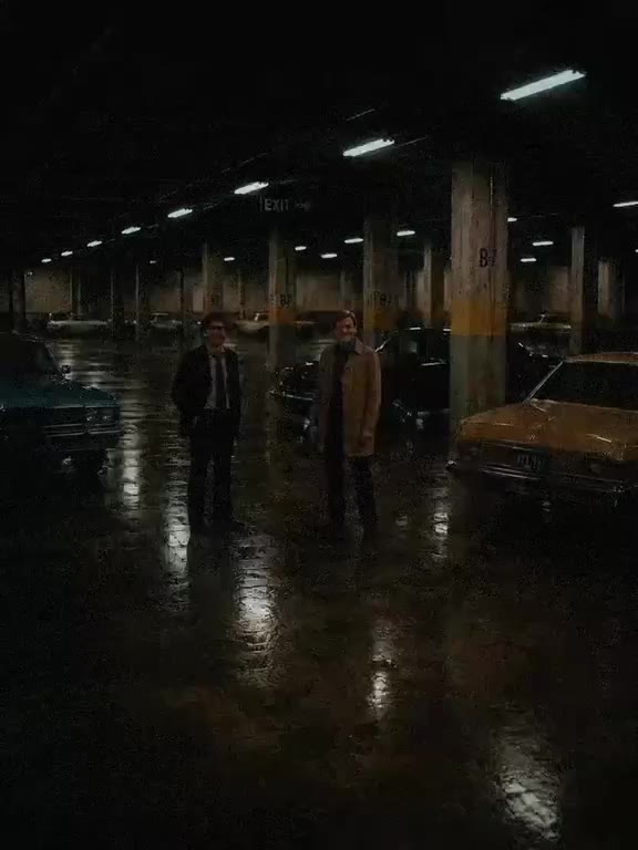 Two men face each other in a rain-slick underground car park at night.